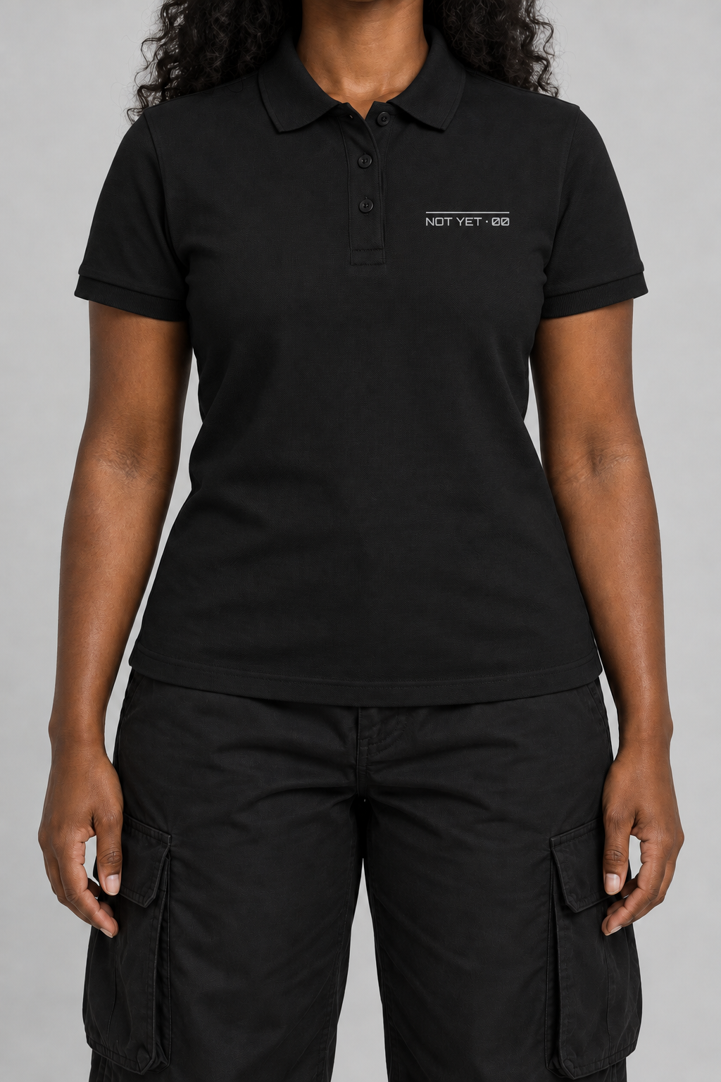 black pique polo with a small light-grey NOT YET 00 line on the chest, on model, front view from the collarbone down