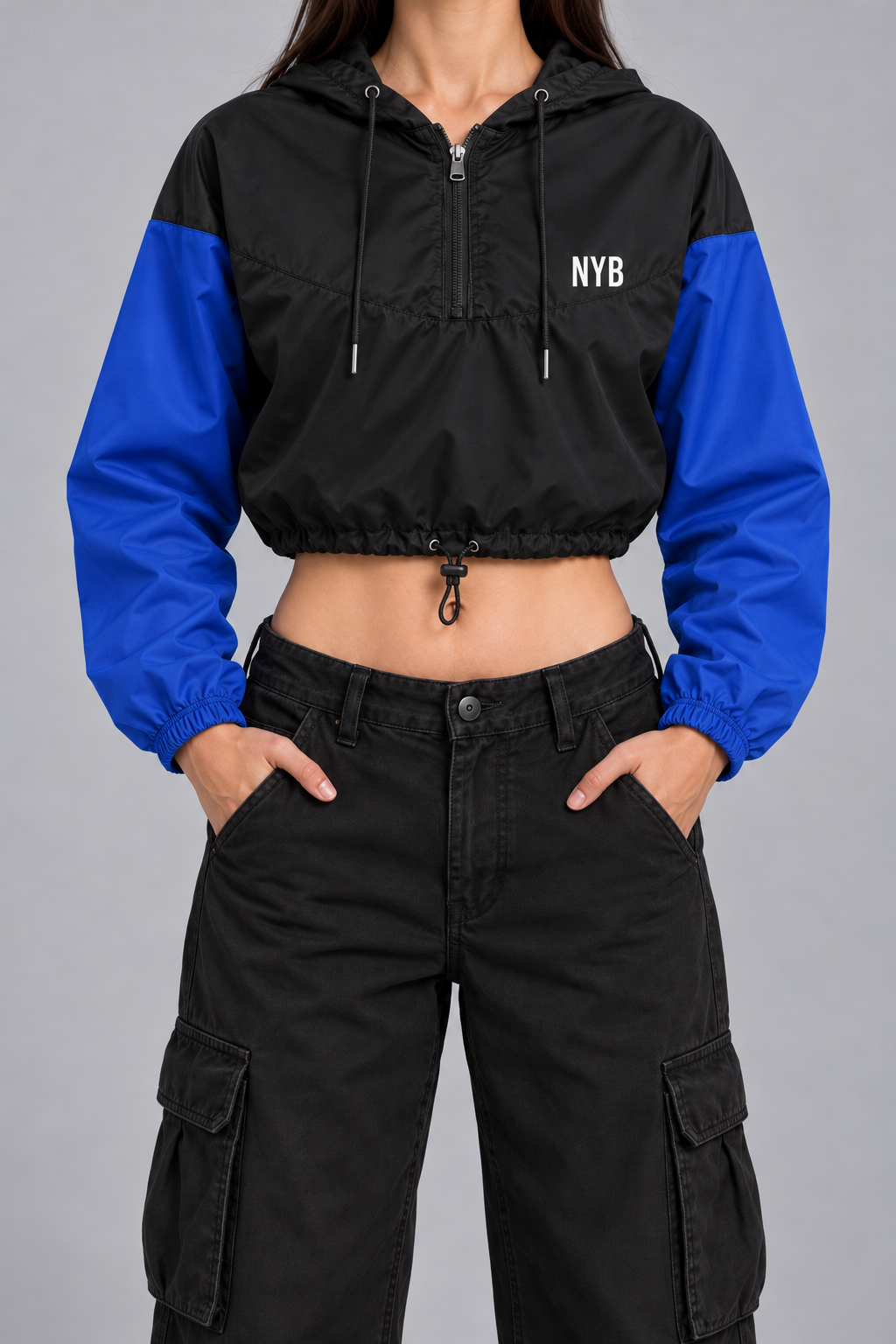 cropped half-zip windbreaker, black with cobalt blue sleeves and a small white NYB on the chest, on model, front view from the collarbone down with hands in the trouser pockets