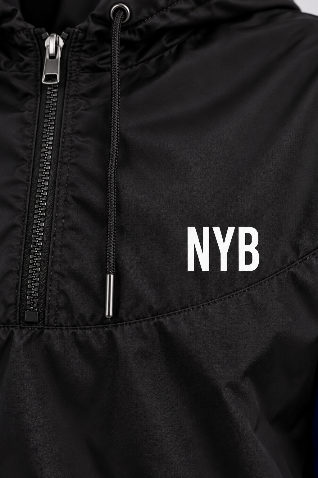 cropped half-zip windbreaker, black with cobalt blue sleeves and a small white NYB on the chest, close-up of the zip, drawcord and white NYB