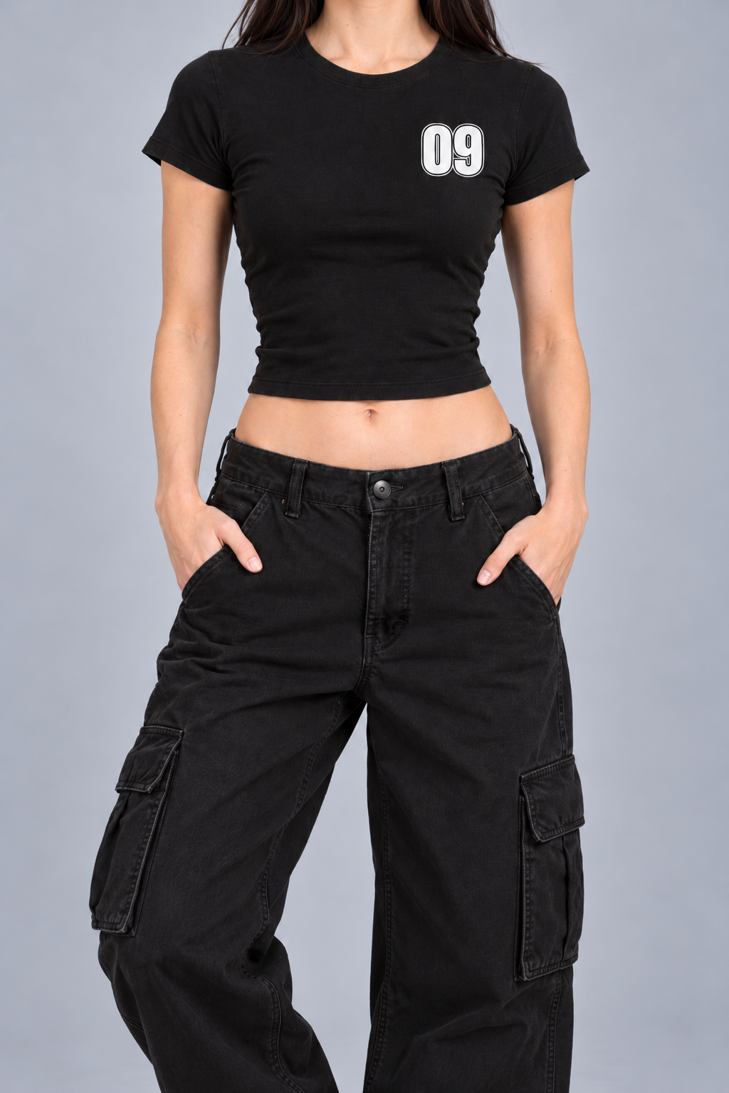 black fitted baby tee with a small white varsity 09 on the left chest, on model, front view from the collarbone down with hands in the trouser pockets