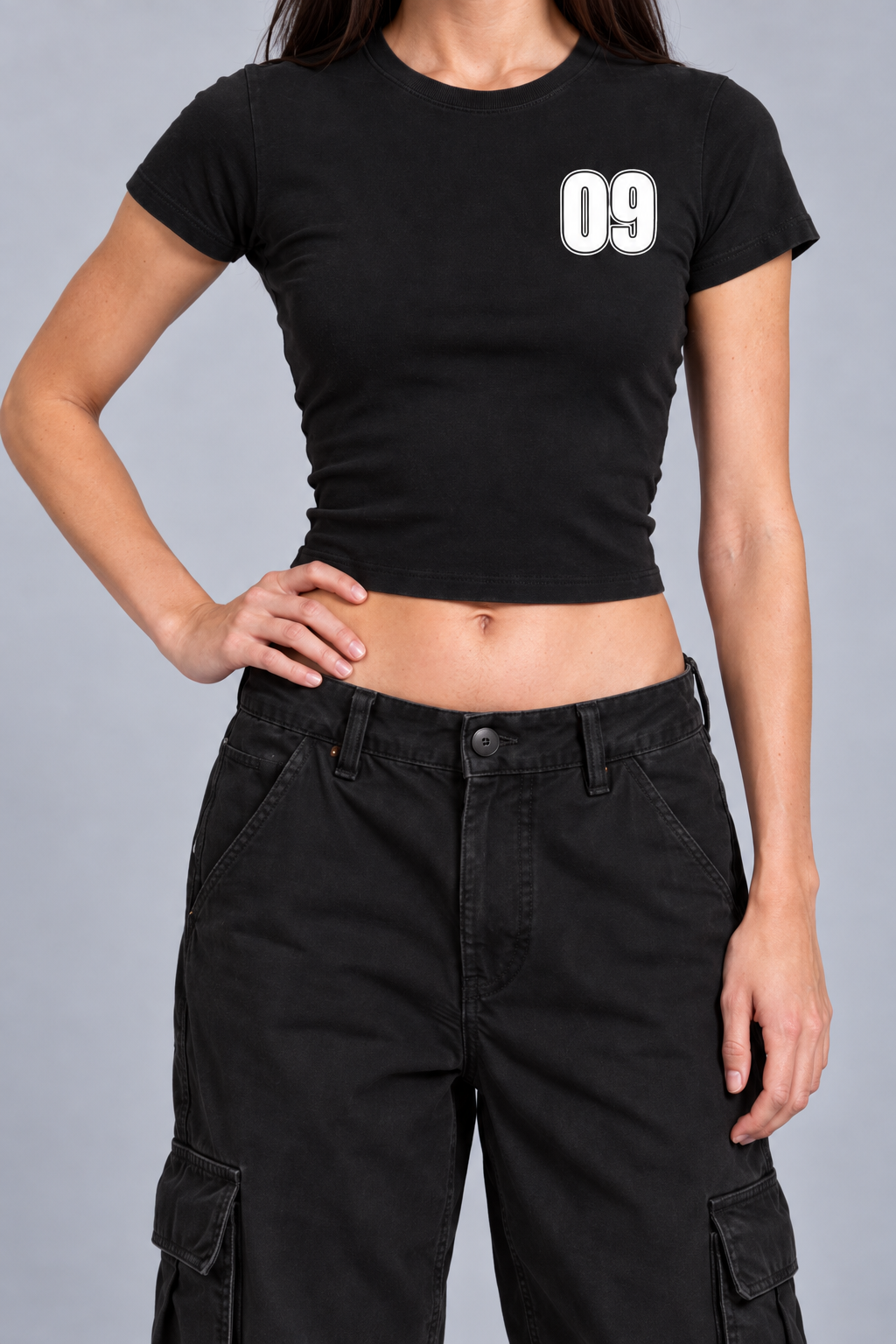 black fitted baby tee with a small white varsity 09 on the left chest, on model, front view from the collarbone down with one hand on the hip