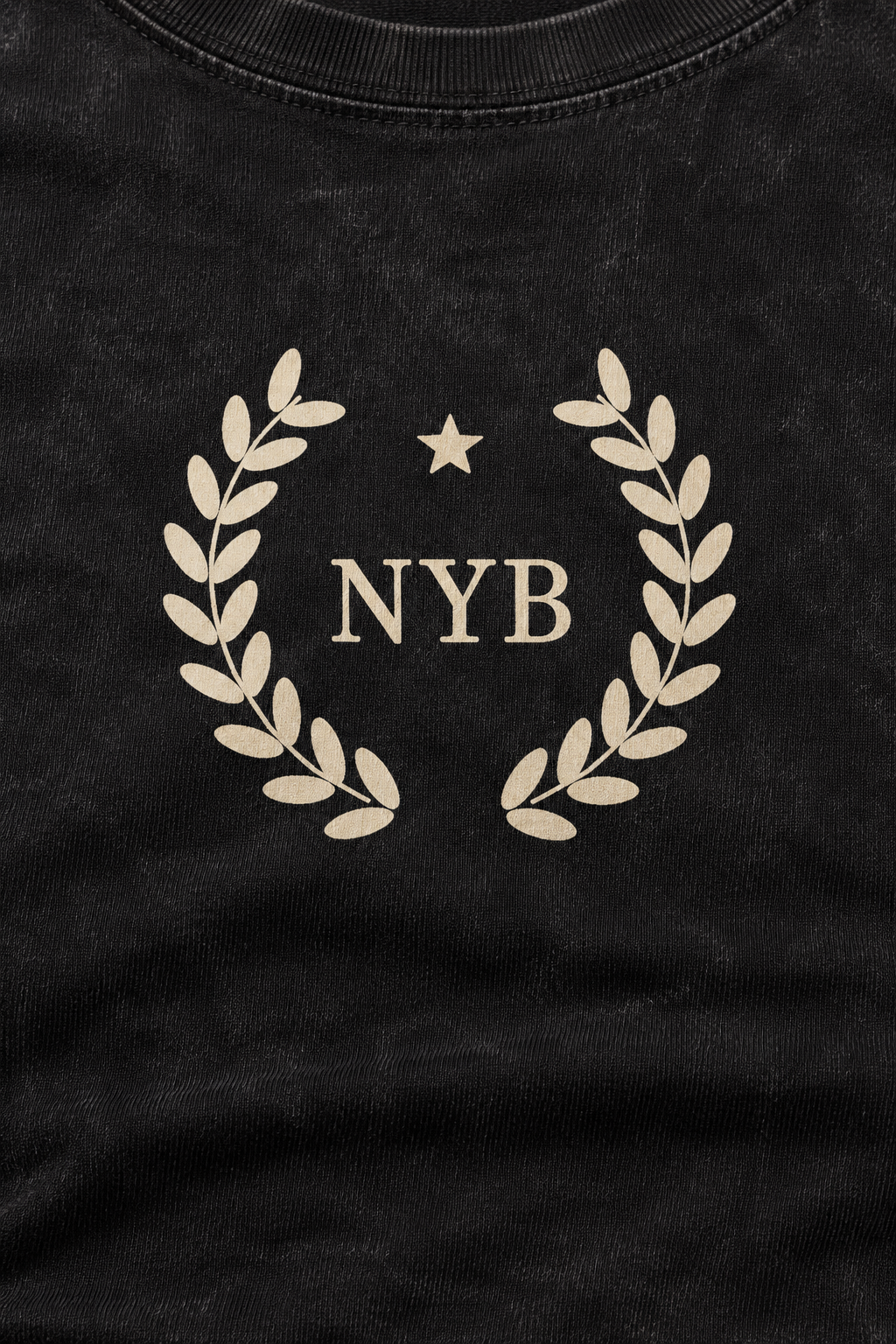 snow-washed black crop tee with a small cream laurel crest reading NYB on the chest, close-up of the cream laurel crest and NYB on the snow-washed cotton