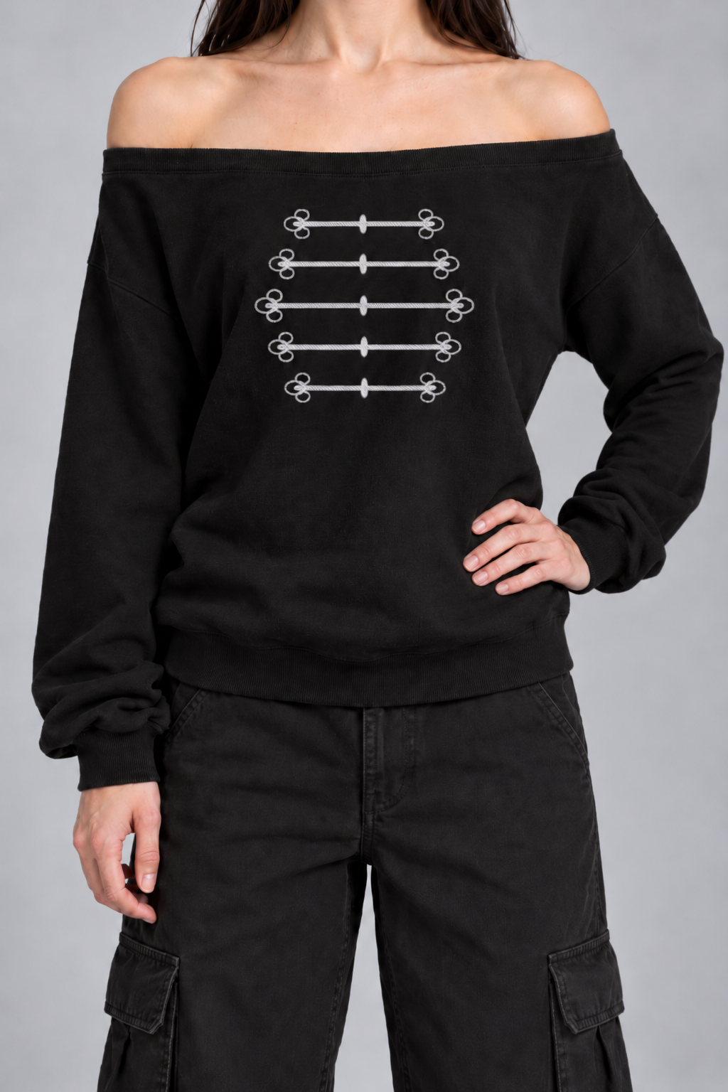 black off-shoulder sweatshirt with silver-grey military frogging across the chest, on model, front view from the collarbone down with one hand on the hip