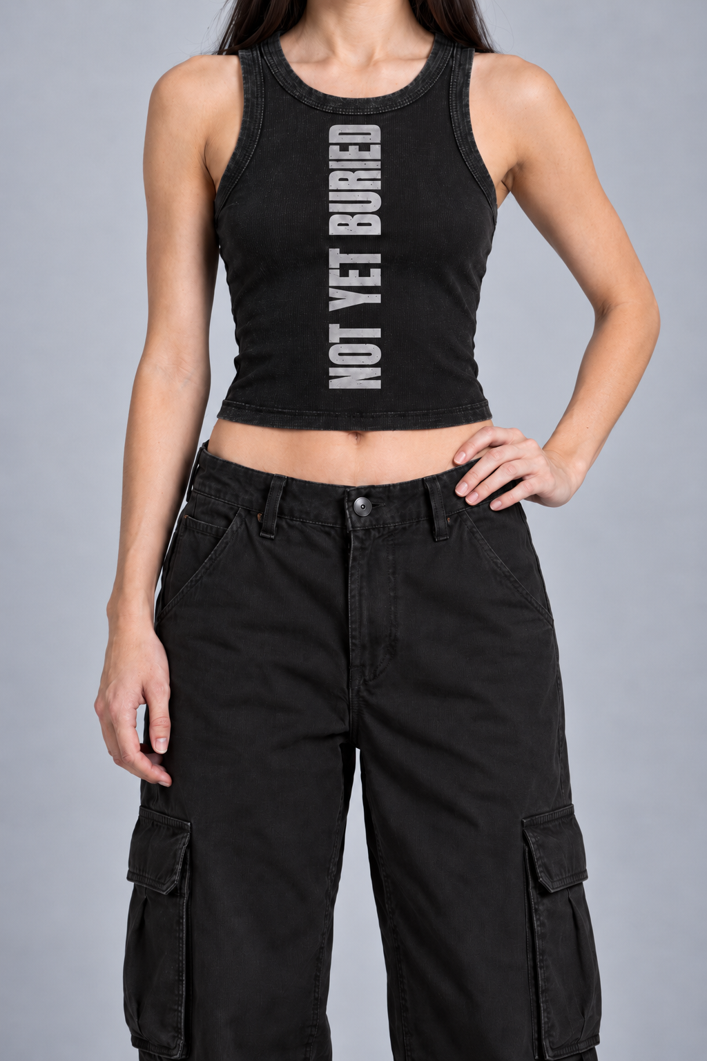 snow-washed black tank with NOT YET BURIED in tall silver-grey letters running up the front, on model, front view from the collarbone down with one hand on the hip
